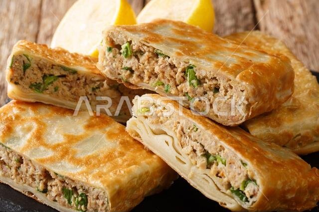 طبق طبق سعودي شعبي، يتكون من اللحم والبيض والبصل الأخضر، معروض على لوح خشبي فوق الطاولة. (صورة أفقية)