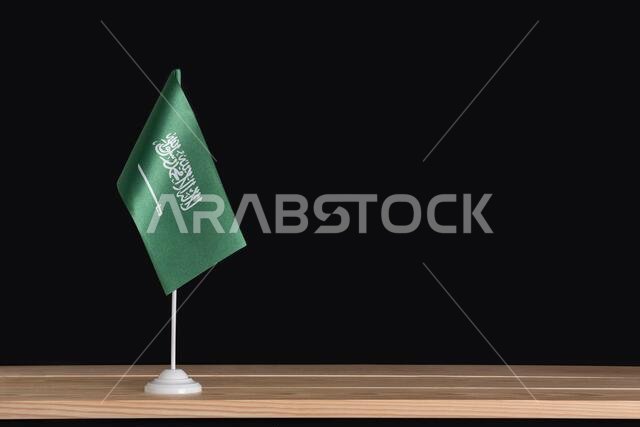 National flag of Saudi Arabia on table, black background. Green flag with sword. Copy space.
