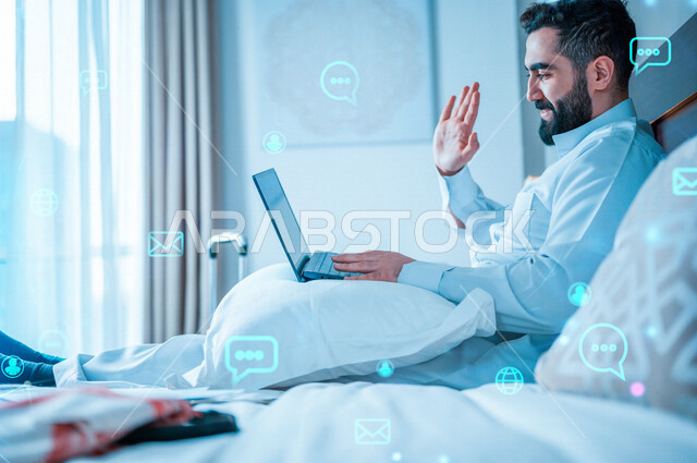 رجل عربي خليجي سعودي يقوم باجراءة مكالمة فيديو من خلال الحاسوب المحمول، اجتماع عمل عن بعد، القاء التحية من خلال شاشة اللابتوب، تقنيات حديثة، دردشة وتواصل، علاقات اجتماعية، سياحة وفندقة , رسومات هولوجرامية .