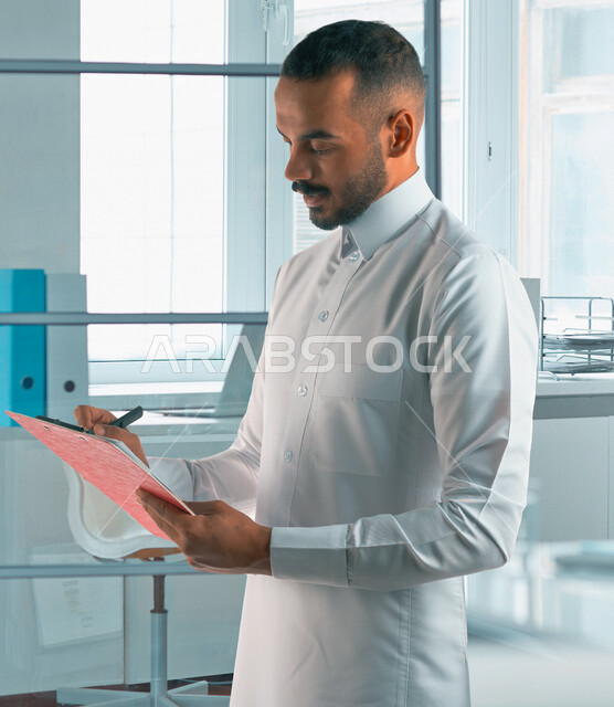 رجل عربي خليجي سعودي يقوم بتدوين الملاحظات على الورق ، التخطيط للعمل ، توقيع عقد عمل ، تدوين نتائج الاجتماع ، اعداد تقارير ومهام العمل ، دراسة جدوى الاعمال