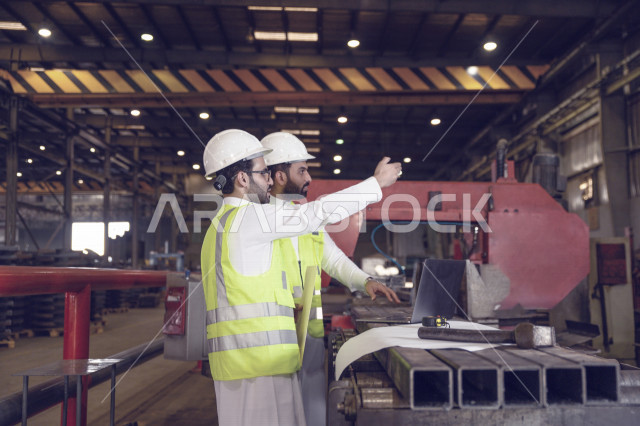 مهندسان مشرفان عربيان خليجيان سعوديان داخل مصنع الحديد ، يحمل احدهم ملف الملاحظات ، تتبع العمل من خلال الحاسوب المحمول و مخطط المصنع ، متابعة سير العملية الانتاجية ،مفهوم الهندسة والتصنيع