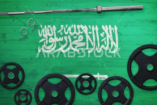 Saudi Arabia gym concept. Top view of heavy weight plates with iron bar on national background.