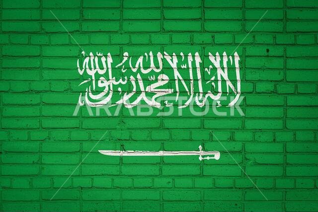 علم المملكة العربية السعودية مرسوم بألوان زاهية على جدار من الطوب القديم. راية علم على خلفية جدار من الطوب.