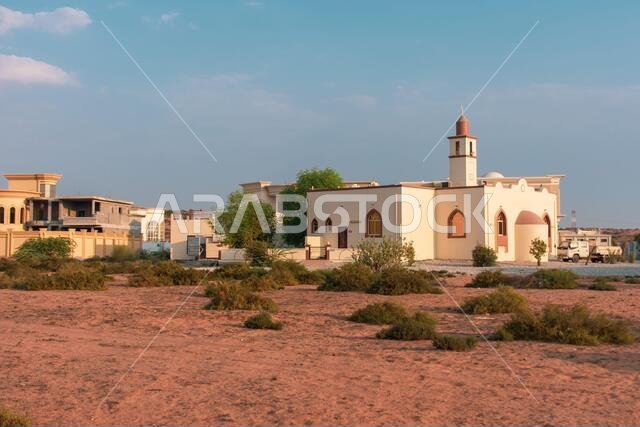 المسجد الأبيض في منطقة سكنية في الشرق الأوسط، تحت سماء زرقاء في ضوء شمس العصر المتأخر.