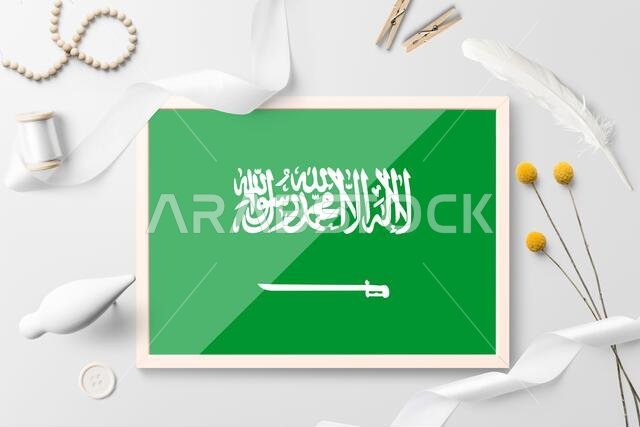 Saudi Arabia flag in wooden frame on white creative background. White theme, feather, daisy, button, ribbon objects.