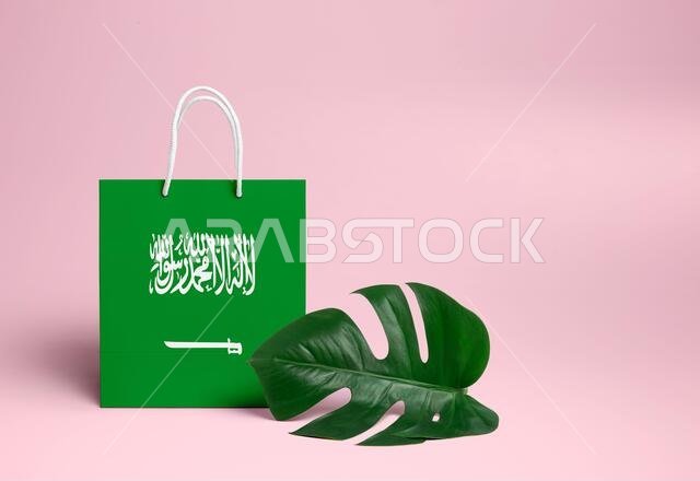 مفهوم التسوق في المملكة العربية السعودية. حقيبة تسوق كرتونية وطنية مزينة بورقة مونستيرا وخلفية وردية. موضوع التسوق الإلكتروني.