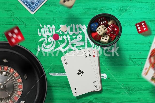 موضوع كازينو في المملكة العربية السعودية. أوراق لعب البوكر، ورقائق وبطاقات على طاولة حمراء مع خلفية العلم الوطني. قمار ومراهنات.