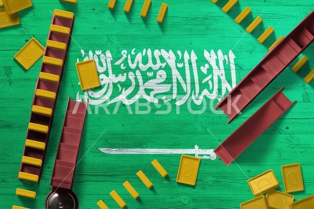 علم المملكة العربية السعودية على خلفية وطنية مع قطع الدومينو على طاولة خشبية. منظر علوي. فكرة اللعبة. علم المملكة العربية السعودية على خلفية وطنية مع قطع الدومينو على طاولة خشبية. منظر علوي. فكرة اللعبة.