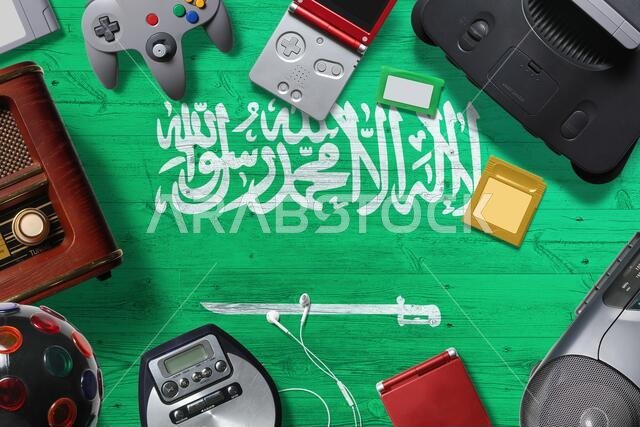 مفهوم ألعاب الفيديو القديمة في المملكة العربية السعودية. مجموعة من أجهزة التحكم بألعاب الفيديو القديمة تم تصويرها من الأعلى على خلفية وطنية.