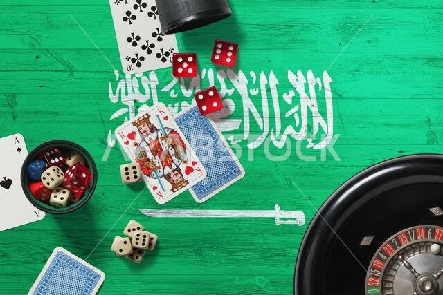 موضوع كازينو في المملكة العربية السعودية. أوراق لعب البوكر، ورقائق وبطاقات على طاولة حمراء مع خلفية علم خشبي وطني. قمار ومراهنات. موضوع كازينو في المملكة العربية السعودية. أوراق لعب البوكر، ورقائق وبطاقات على طاولة حمراء مع خلفية علم خشبي وطني. قمار ومراهنات.