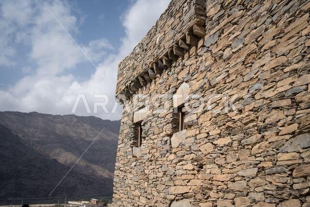 Exterior of ancient stone wall of historic building of Marble Village in Al Bahah against background of rocky terrain and cloudy sky in summer in Saudi Arabia