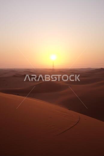 صورة لشروق شمس خلاب في الصحراء العربية، مع برج لنقل الطاقة، في الرياض، المملكة العربية السعودية. أمل، بدايات جديدة، غدٌ أكثر إشراقاً.