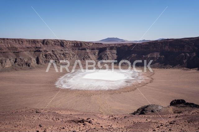 Aerial view of white sodium phosphate crystal surface placed inside maar crater at bright sunlight against blue clear sky and mountains