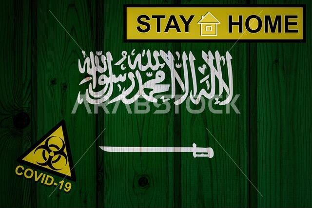 علم المملكة العربية السعودية بأبعاده الأصلية. الحجر الصحي والعزل - ابقَ في المنزل. علم يحمل رمز الخطر البيولوجي ونقش كوفيد-19.