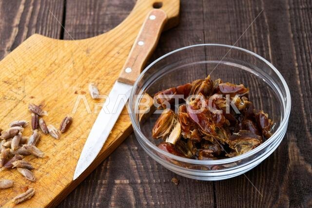 حمص - حليب التمر، طبق رمضاني تقليدي، طريقة التحضير، المكونات، تمر منزوع النوى في طبق، سكين وبذور على لوح تقطيع على طاولة خشبية