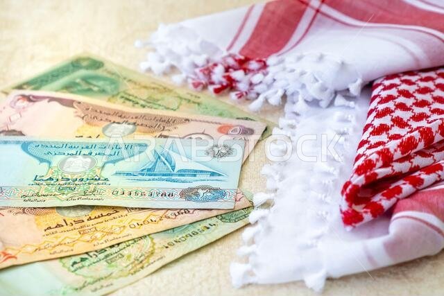 العملات العربية: درهم إماراتي، أوراق نقدية، ووشاح رجالي عربي تقليدي - كوفية عن قرب.
