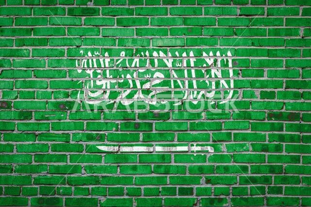 علم المملكة العربية السعودية مرسوم بألوان زاهية على جدار من الطوب القديم. راية علم على خلفية جدار من الطوب.