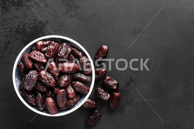 تمر مجفف في وعاء على خلفية سوداء مع مساحة فارغة للنص، منظر علوي. نسيج خلفية خرسانية سوداء
