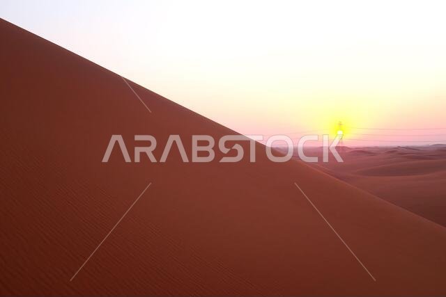 شروق الشمس بألوان الباستيل على الكثبان الرملية الحمراء لصحراء الدهناء في الرياض، المملكة العربية السعودية. بدايات جديدة، رمز للأمل ومستقبل أكثر إشراقاً.