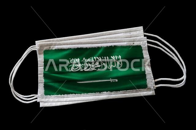 كمامات جراحية مطبوع عليها علم المملكة العربية السعودية. معزولة على خلفية سوداء. مفهوم استخدام الكمامات في الجهود السعودية لمكافحة كوفيد-19
