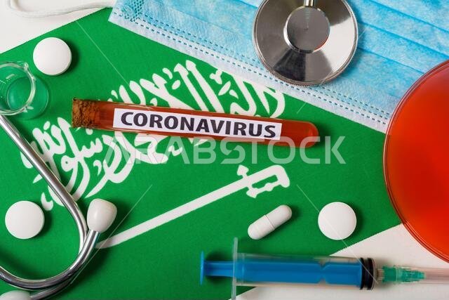 مفهوم فيروس كورونا المستجد (nCoV). قناع تنفس واقٍ، سماعة طبية، محقنة، أقراص، من الأعلى، على علم المملكة العربية السعودية. تفشٍ جديد للفيروس في الصين.