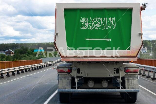 Big  truck with the national flag of  Saudi Arabia moving on the highway, against the background of the village and forest landscape. Concept of expor