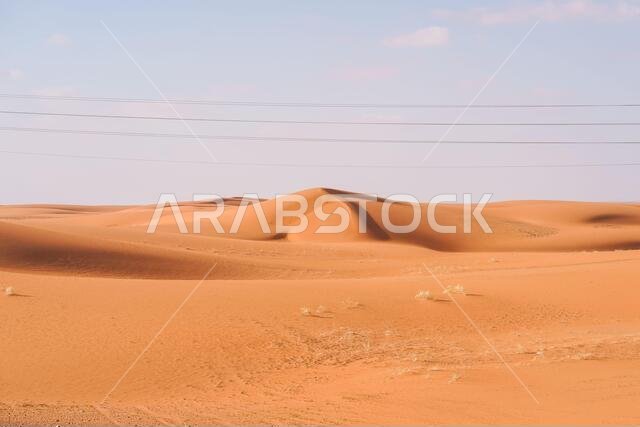 صحراء رائعة ذات كثبان رملية حمراء اللون، تلوح في الأفق فيها خطوط الكهرباء وأعمدة الإنارة في المملكة العربية السعودية