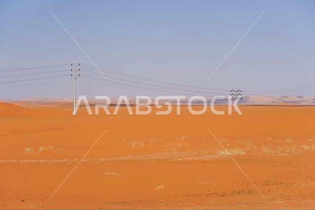 صحراء رائعة ذات كثبان رملية حمراء اللون، تلوح في الأفق فيها خطوط الكهرباء وأعمدة الإنارة في المملكة العربية السعودية