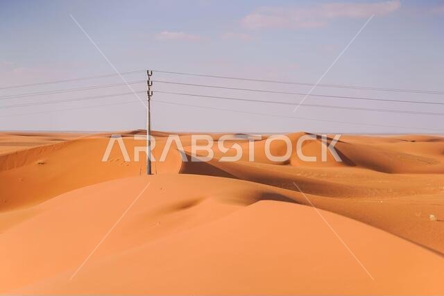 صحراء رائعة ذات كثبان رملية حمراء اللون، تلوح في الأفق فيها خطوط الكهرباء وأعمدة الإنارة في المملكة العربية السعودية