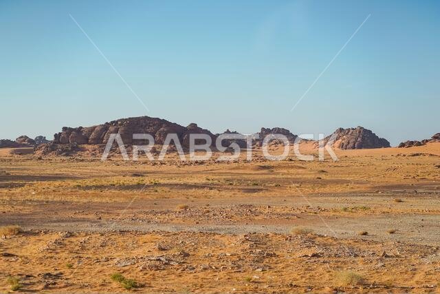 bleak desert landscape of reddish sands with mountain and rock formations in northern Saudi Arabia