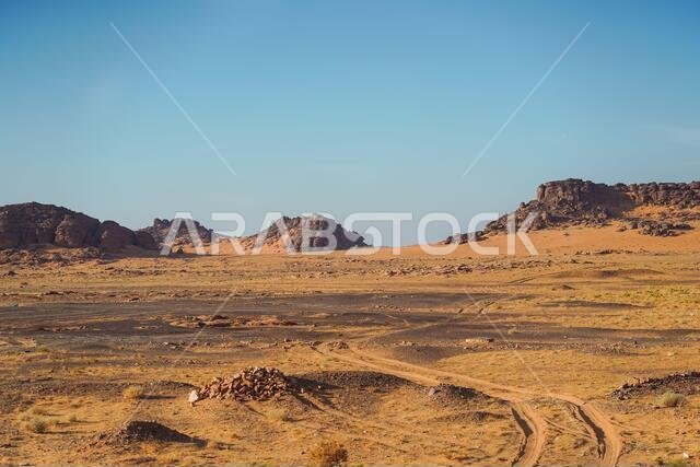 bleak desert landscape of reddish sands with mountain and rock formations in northern Saudi Arabia