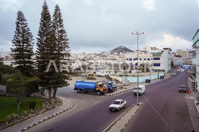 Abha / Saudi Arabia - January 23, 2020: Abha city panorama with trees, oil transport trucks and mountain with lights in the background