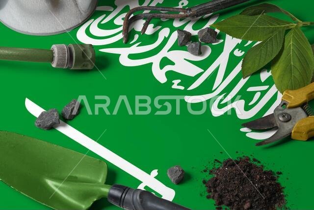 Saudi Arabia flag with gardening tools background on table. Spring in the garden concept with free copy space.