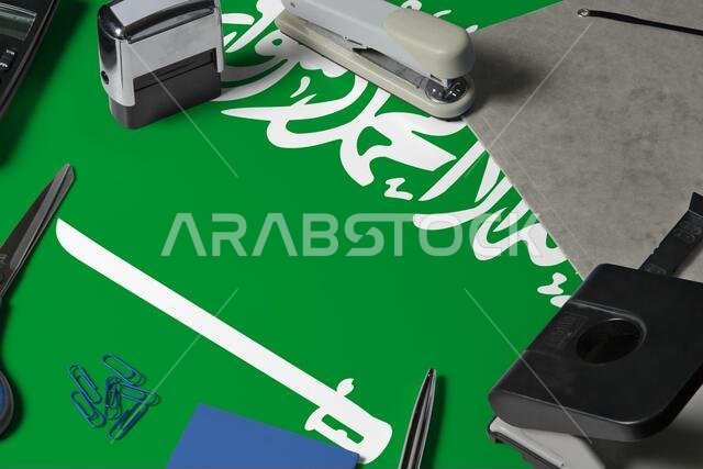 Saudi Arabia flag with office clerk workplace background. National stationary concept with office tools.