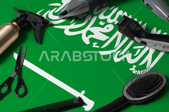 علم المملكة العربية السعودية مع أدوات قص الشعر. أمشاط ومقصات وأدوات تصفيف الشعر على طاولة في صالون تجميل على خلفية خشبية وطنية.