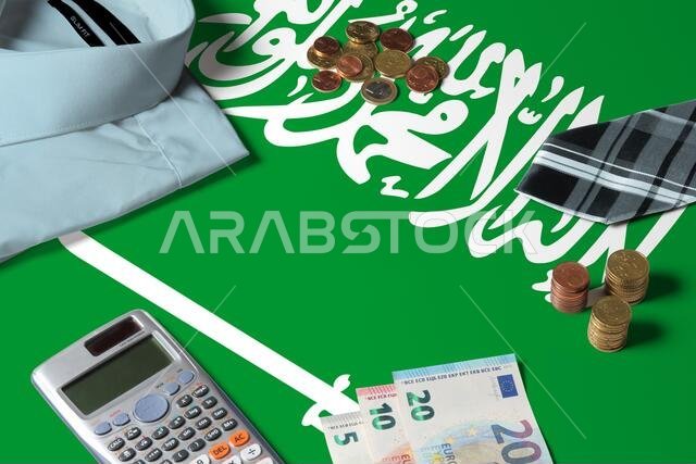 علم المملكة العربية السعودية موضوع على طاولة بتصميم بسيط يجسد مفهوم النقود. عملات معدنية ورموز مالية على سطح العلم. موضوع الاقتصاد الوطني.