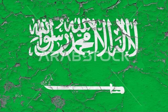 صورة مقربة لعلم المملكة العربية السعودية، متسخ ومتضرر ومتآكل على جدار، يتقشر طلاؤه ليكشف عن سطحه الداخلي. فكرة كلاسيكية.