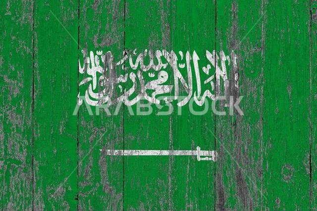 علم المملكة العربية السعودية على سطح خشبي مخدوش. خلفية وطنية عتيقة. طاولة خشبية قديمة عليها علم مخدوش.