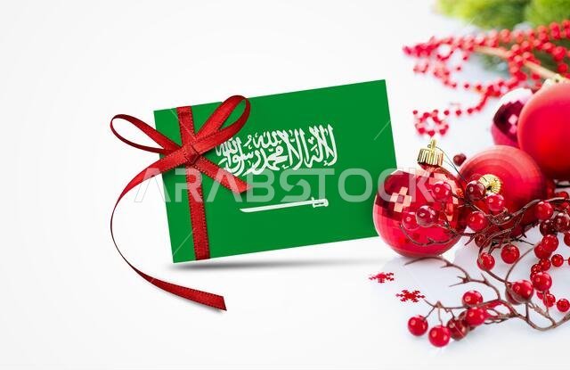 علم المملكة العربية السعودية على بطاقة دعوة رأس السنة الجديدة مع زينة عيد الميلاد الحمراء. تصميم وطني لتهنئة المملكة بالعام الجديد.