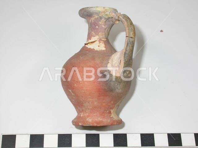 Small jug of white clay with red mud layer. The neck and handle have been broken off and are glued again. The handle consisted of three strips of clay of which the outer two are almost completely broken., Crockery, earthenware, H 8.1 cm, D bottom 3.5 cm, D edge 2.3 cm., Late Bronze Age? 1600-1200 BC, Saudi Arabia