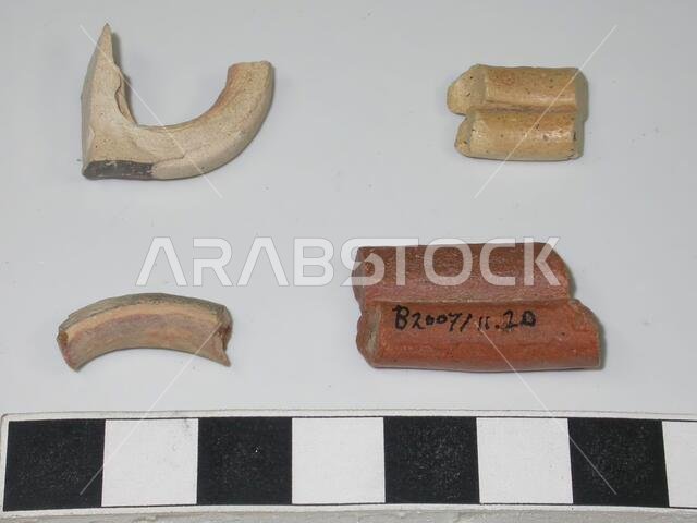 أربع شظايا من أجزاء أباريق فخارية. جميعها كانت جزءًا من أجزاء تحتوي على أكثر من شريط طيني متجاور. ثلاث شظايا من الطين الأبيض (اثنتان منها مزخرفتان باللون الأسود) وشظية واحدة من الطين الأحمر. فخار، أكبرها: الطول 2.7 سم، أصغرها: الطول 1.4 سم، العرض 1.1 سم. العصر البرونزي المتأخر؟ 1600-1200 قبل الميلاد، المملكة العربية السعودية