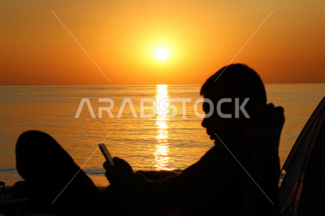 صورة ظلية لرجل يجلس أمام شاطئ البحر ، جمال منظر الغروب في سماء المملكة العربية السعودية ، جلسات هادئة ، هدوء وجمال البحر ، غروب الشمس على شاطئ بحر السعودية