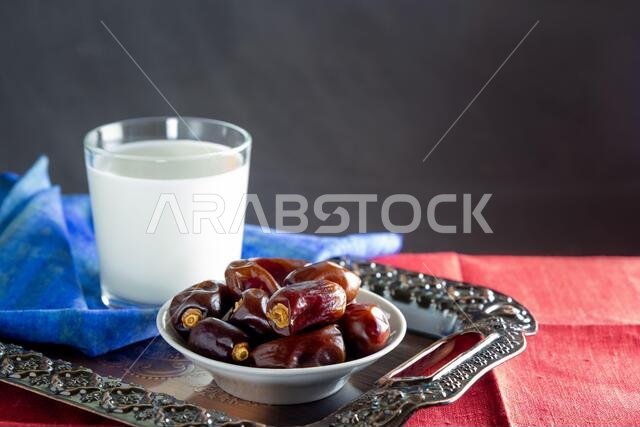 Dates and a glass of milk on metal tray and colorful napkins. Ramadan, Iftar food concept. Dark background, copy space