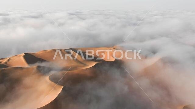 Aerial view of a massive sand dune surrounded by winter morning fog cloud in Empty Quarter. Liwa desert, Abu Dhabi, United Arab Emirates.