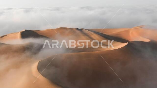 صورة جوية لكثيب رملي ضخم محاط بسحابة ضباب صباحية شتوية في الربع الخالي. صحراء ليوا، أبوظبي، الإمارات العربية المتحدة.