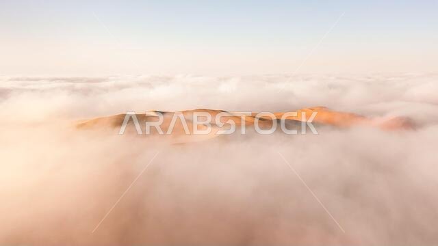 Aerial view of a massive sand dune surrounded by winter morning fog cloud in Empty Quarter. Liwa desert, Abu Dhabi, United Arab Emirates.