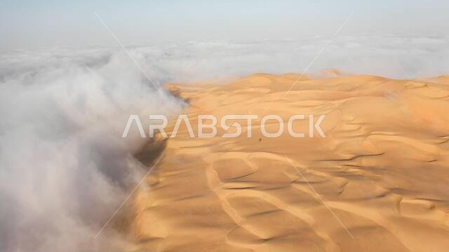 Aerial view of a massive sand dune surrounded by winter morning fog cloud in Empty Quarter. Liwa desert, Abu Dhabi, United Arab Emirates.