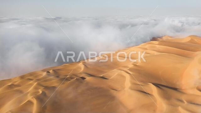 Aerial view of a massive sand dune surrounded by winter morning fog cloud in Empty Quarter. Liwa desert, Abu Dhabi, United Arab Emirates.