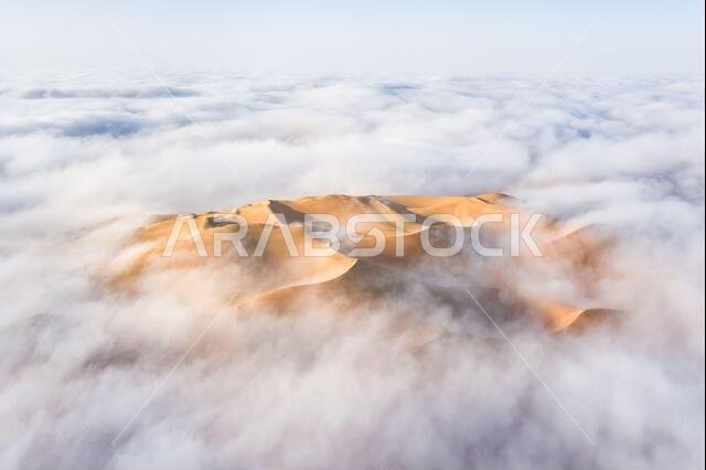 Aerial view of a massive sand dune surrounded by winter morning fog cloud. Liwa desert, Abu Dhabi, United Arab Emirates.
