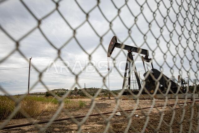 Oil Pump in Cloudy Rough Weather with Chain Link Fence